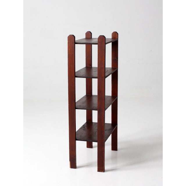 An early 20th century wood etagere with a narrow, upright profile and a quiet, structured presence. Four open shelves are...