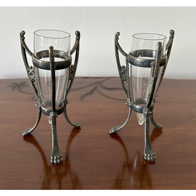 Coppia di piccoli portafiori in silverplated, con vasche in vetro originali e fusti cesellati a motivi vegetali con piedi...