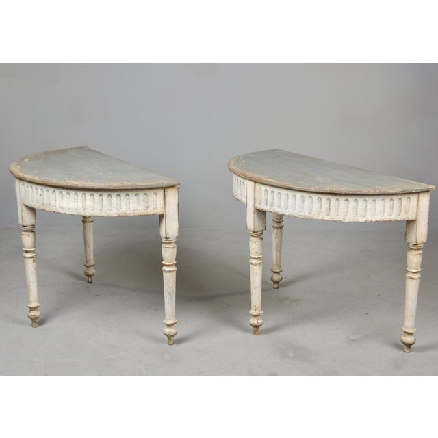 Found in Sweden, this pair of painted demilune console tables dates from the 1880s. The softly worn, creamy white bases...