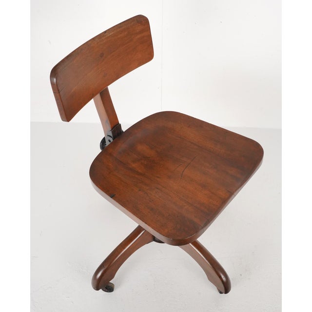 Vintage walnut swivel office chair featuring a contoured, saddled seat and a broad, curved backrest. The chair has an...