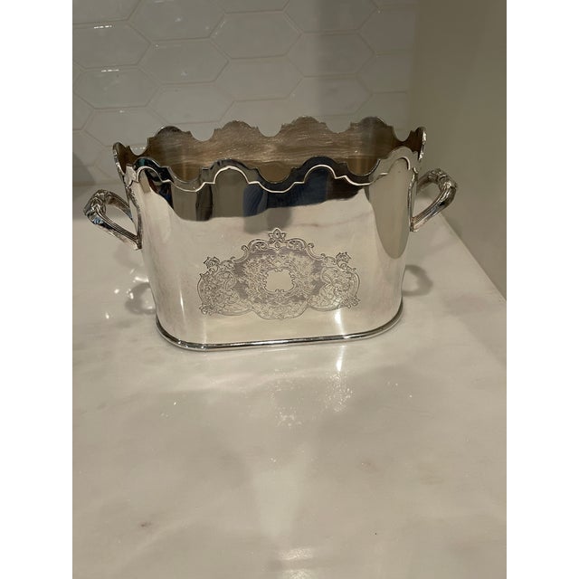 Vintage silverplated wine caddy with scalloped edges and elaborate handles. There are engraved heraldic shields on the...