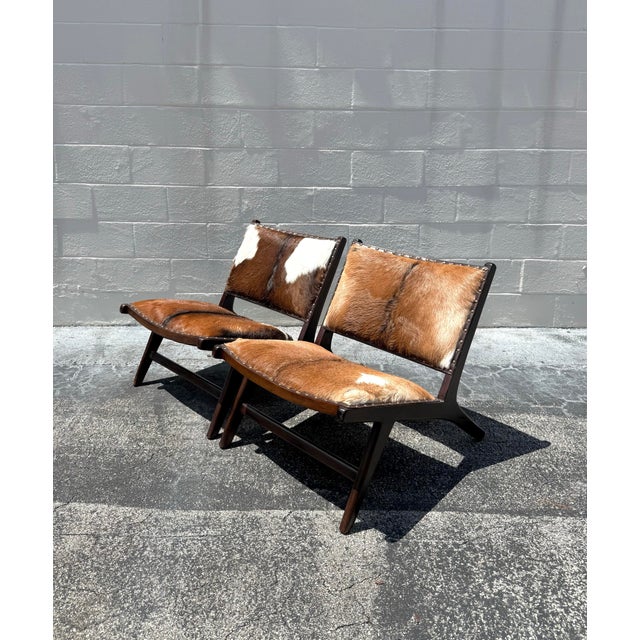 A sculptural pair of contemporary safari lounge chairs featuring rich hair-on-hide upholstery over dark stained wood...