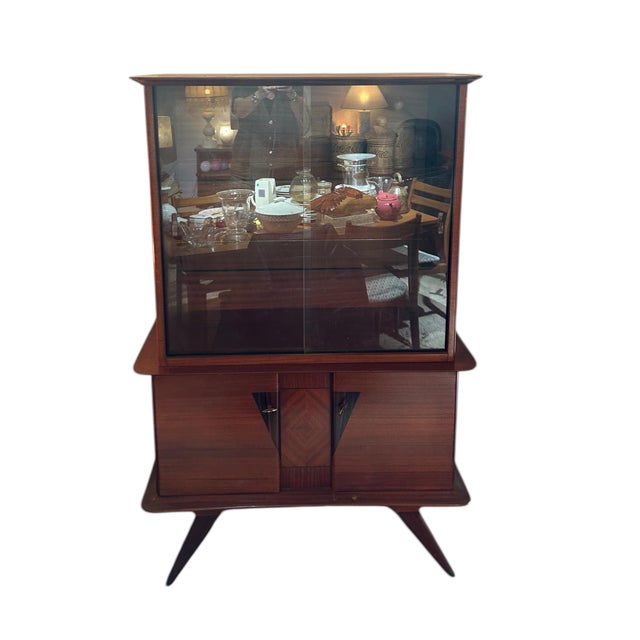 Elegant 1950s display cabinet, most likely of Italian origin. This piece features a wood frame with warm-toned veneers,...