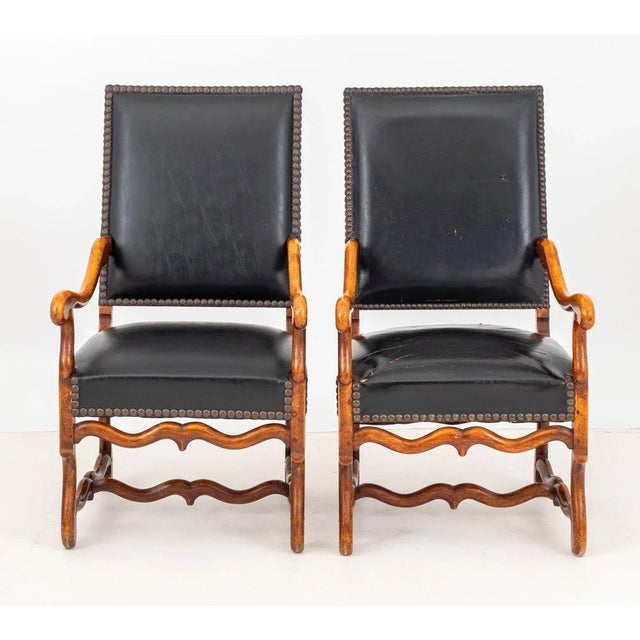 Pair of Louis XIV Style Walnut Fauteuil, with riveted black leather upholstery on four carved wood legs conjoined by...