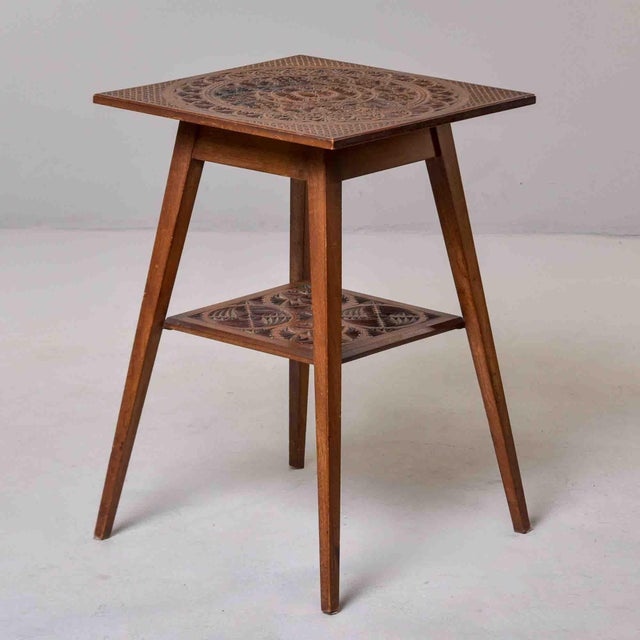This two-tier occasional table features a square top and a smaller square lower shelf, both densely chip-carved in a...