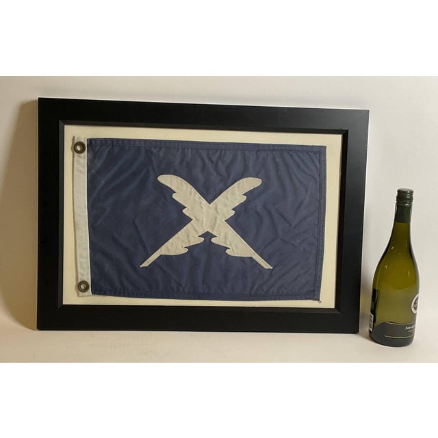 Nautical flag in frame with glass. Blue flag with crossed feathered quills. Blue field with white applied letters. White...
