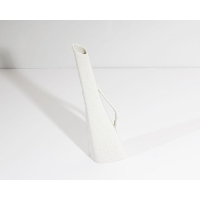 A white porcelain bud vase produced by Hutschenreuther Selb. Made in Germany, this vase has a handle on one side and a...