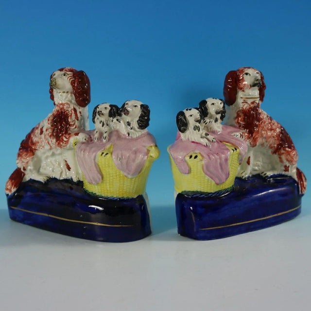 Pair of Staffordshire Pottery groups which feature a spaniel and her pups in a wicker wash basket, seated on an oval base....