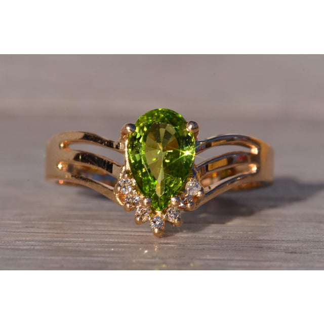 The Equa: Peridot and Natural Diamond Ring in Yellow Gold. This striking ring showcases a central pear brilliant cut...