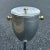 Vintage lidded ice bucket rendered in aluminum with brass finished hardware and plastic liner mounted on chrome stand. Can...