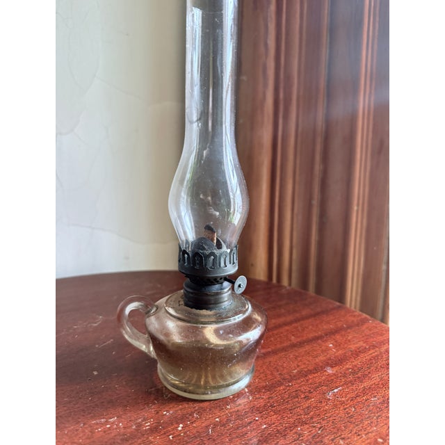 Antique glass finger lamp (chamber lamp) with side finger loop handle for carrying. Clear glass reservoir with squat base...