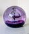 Glass paperweight made in Scotland, features a silver spaceship hovering above the moons craters. in a rich purple color