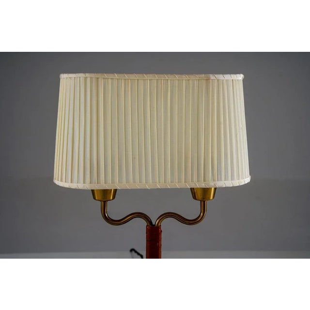 A refined swedish table lamp by asea, featuring a brass double-arm construction with a central leather-wrapped stem and a...