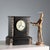 Table clock in engraved black marble with brecciated marble details. Enamelled metal dial decorated with a painted...