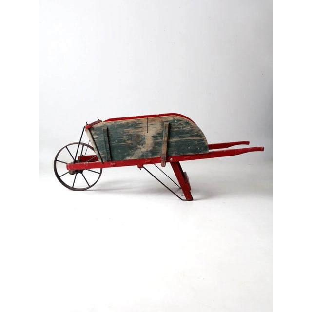 This is an antique wooden wheelbarrow. The rustic red cart features removable green wood sides and an iron wheel.