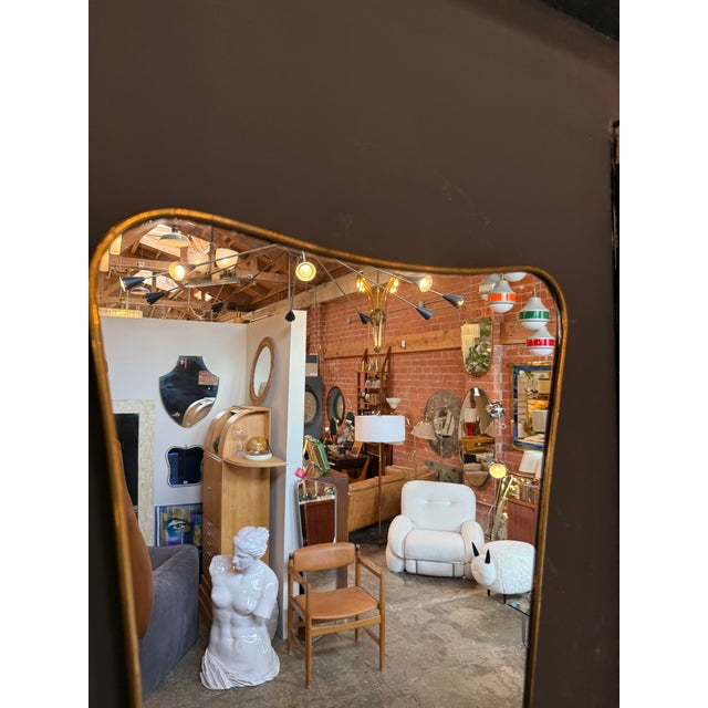 Elegant Italian wall mirror featuring a slender brass frame and an organic, asymmetrical silhouette. Its softly curved...
