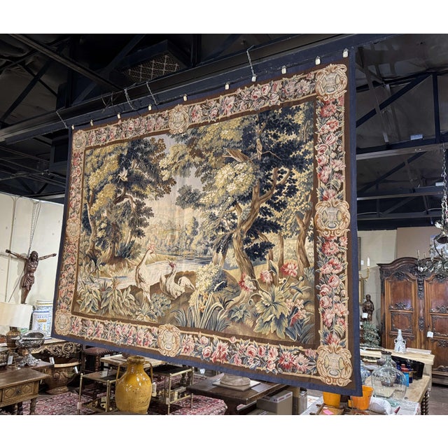 This antique French Aubusson verdure tapestry was handwoven circa 1870 and depicts a lush wooded landscape animated by...