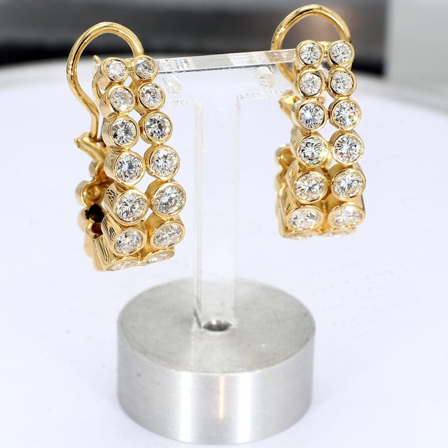 This pair of 18k yellow gold elongated hoop earrings, set with eighteen bezel-set diamonds across two rows going down each...