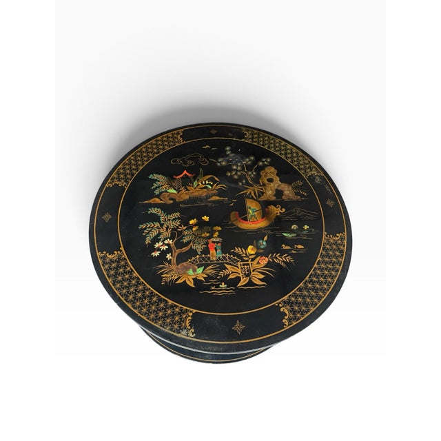 A striking vintage Chinoiserie round side table featuring a black lacquer-style finish, elaborate Asian-inspired landscape...