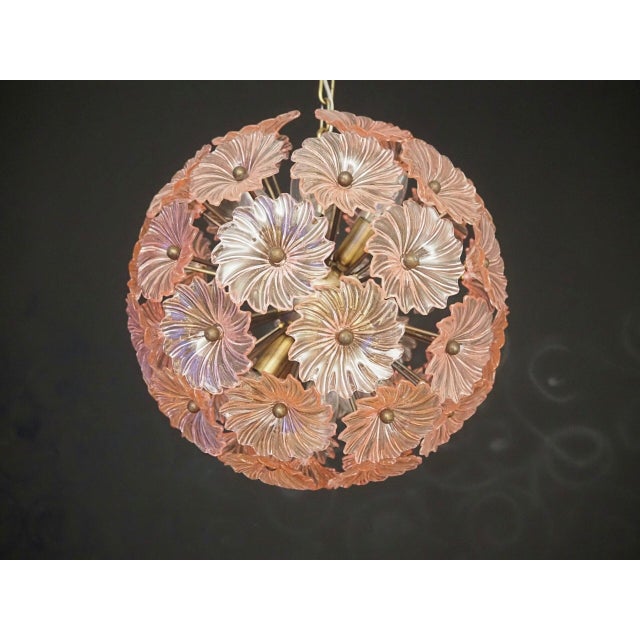 Sputnik chandelier with 51 pink glass daisy-shaped elements, supported by a burnished brass structure. The flowers' fluted...