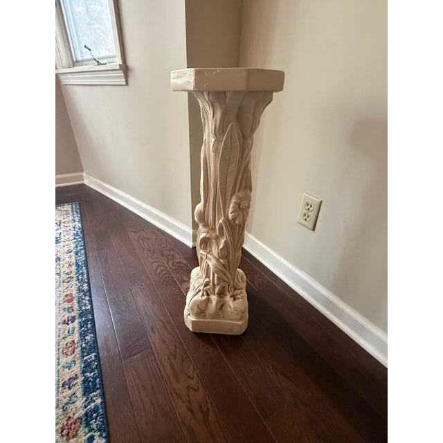 Plaster pedestal stand features an intricate relief of blooming flowers and lush foliage, finished in a soft cream tone...