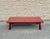 A low coffee table with a red lacquer finish featuring a repeating pattern beneath the surface. The smooth lacquered top...
