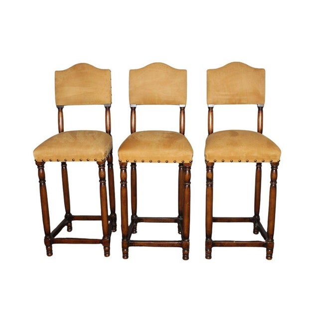 A stylish set of three vintage barstools with suede leather seats showcasing a warm, naturally aged patina. Timeless in...