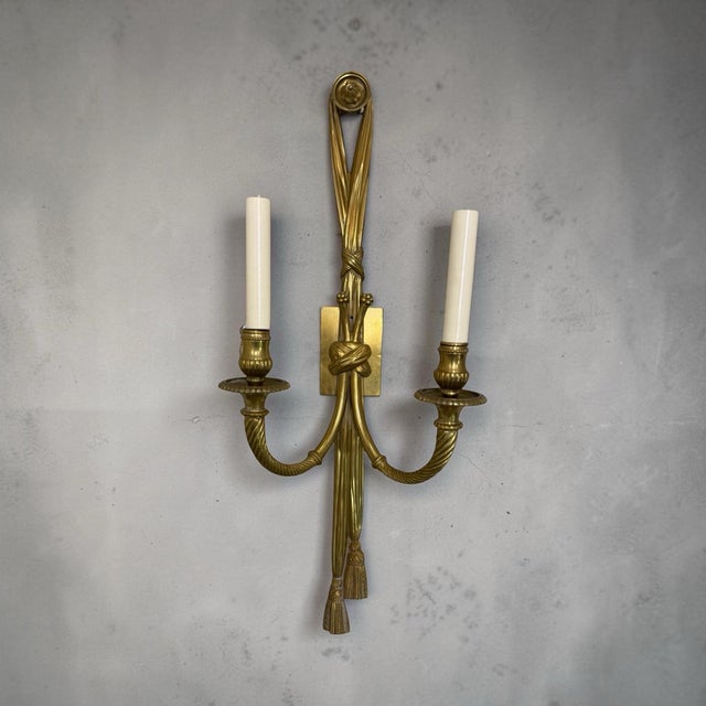 A pair of electrified gilt brass sconces in the timeless French Neoclassical style. Tassle-forms bound and draped, holding...