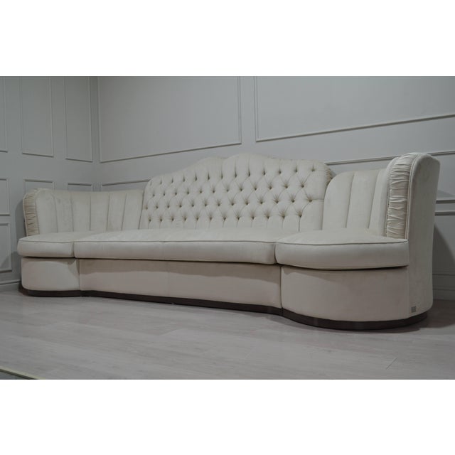 A sophisticated statement sofa combining a gently arched, diamond-tufted backrest with sculptural channelled arms and...