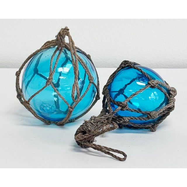 Vintage pair of inspired glass fishing buoys with hand-tied rope net and handle. Hand-blown aqua blue glass. Small buoy...