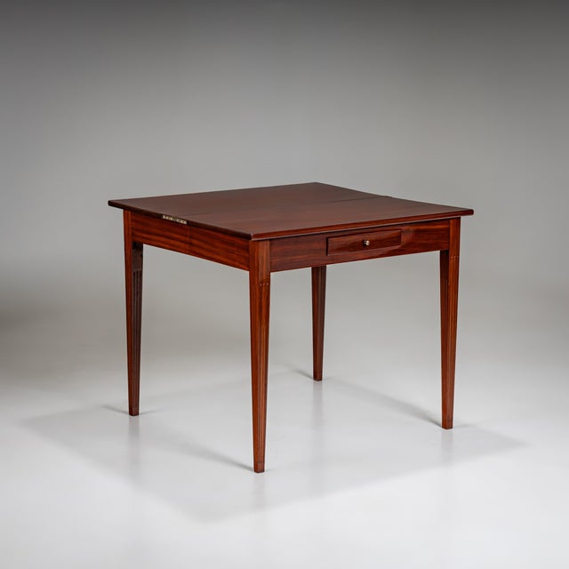Elegant folding table featuring tall, fluted, tapering legs and a narrow drawer integrated into the otherwise smooth...