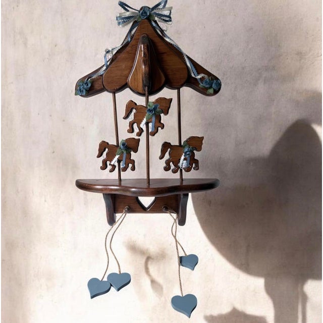decorative wooden wall shelf resembles a vintage carousel, featuring a canopy top, three cut-out carousel horses adorned...