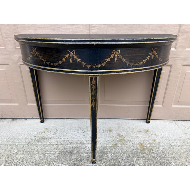 A beautiful Adam or Regency style painted black and gold demilune console table with classically painted details of swags...