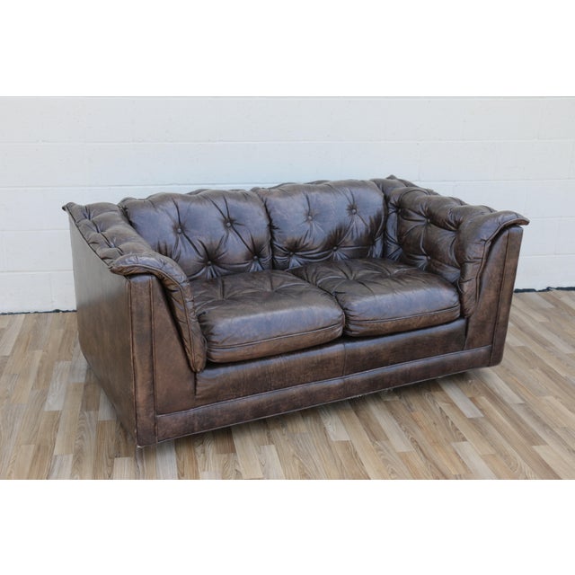 A timeless vintage 1970s Chesterfield loveseat, beautifully upholstered in rich brown leather with classic deep button...