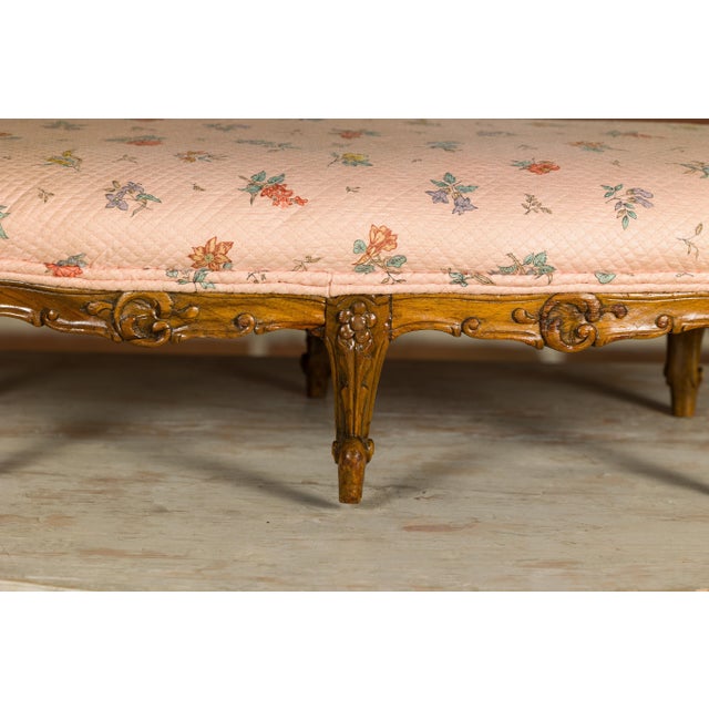 A French Louis XV style wooden footstool from the 19th century with six carved cabriole legs and upholstery. Indulge in...