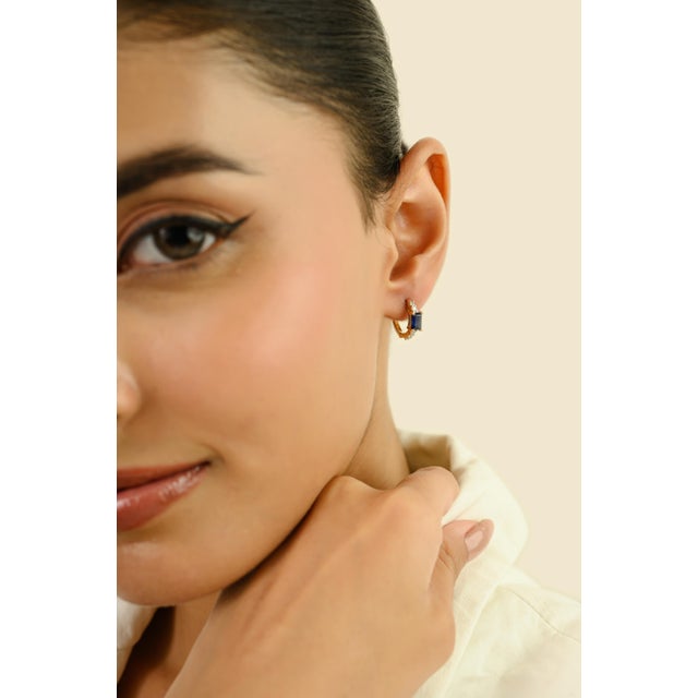 These elegant huggie hoop earrings feature 2 emerald cut blue sapphires totaling 1.03 carats, set in 14K yellow gold. Each...