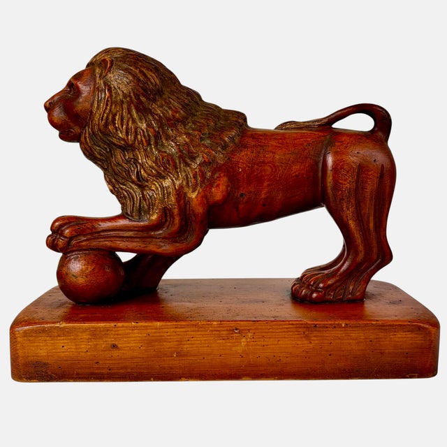 This beautifully carved wood lion stands in a classic pose, with one paw resting on an orb, atop a rectangular plinth. It...