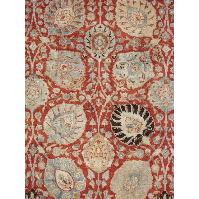 This early 20th-century Persian Tabriz rug presents a richly ornamented allover floral composition across a warm red...