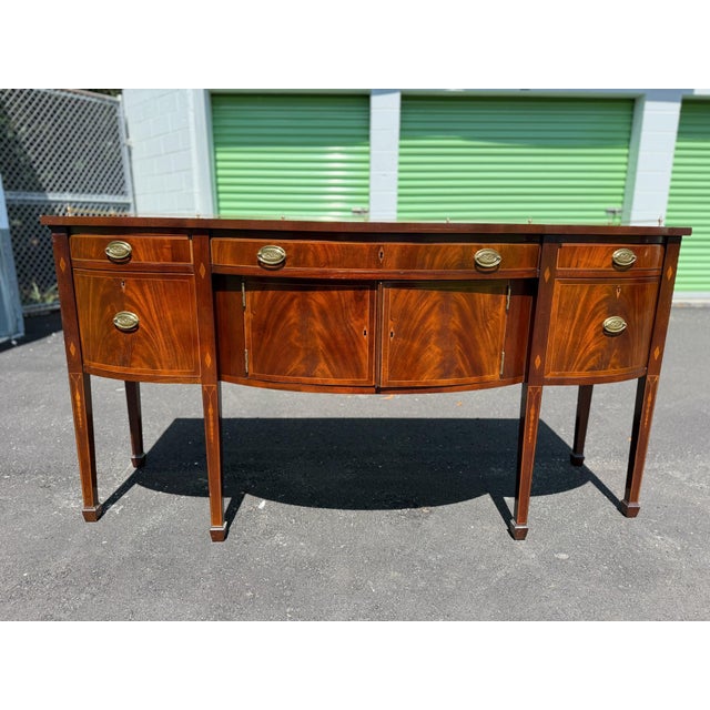 Elegant mahogany sideboard has a serpentine front with decorative wood inlays. This piece features three top drawers and...