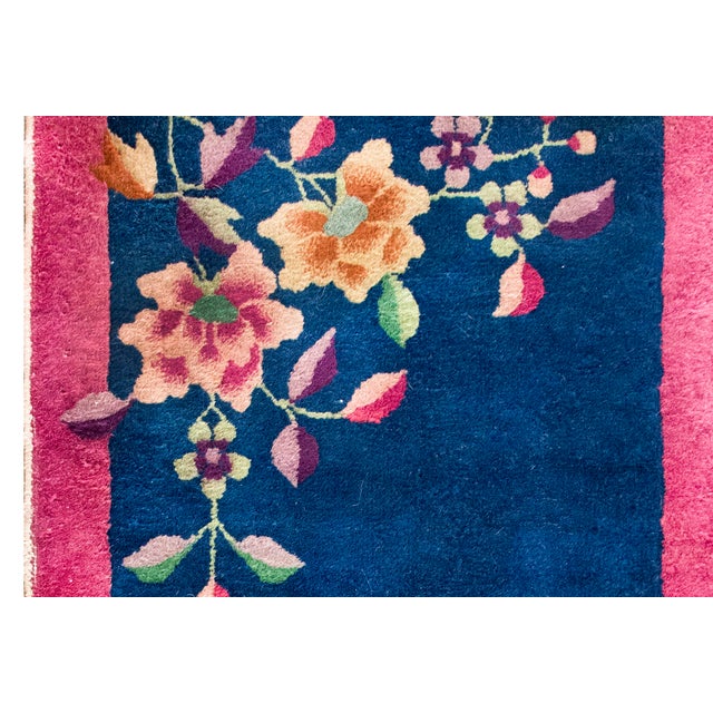 This vintage Chinese Art Deco rug from the 1930s features a vibrant, deep blue field framed by a striking magenta-pink...