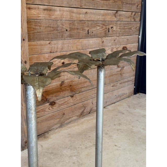 Striking pair of sculptural metal candlestick holders featuring dramatic palm leaf forms atop tall, architectural columns....