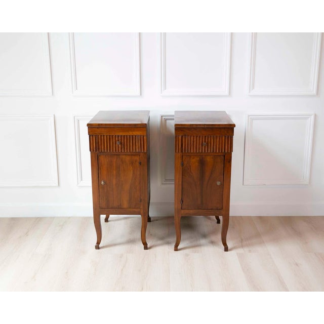A pair of Italian walnut bedside chests from the 18th century with carved fluted drawer, single door and curving legs....