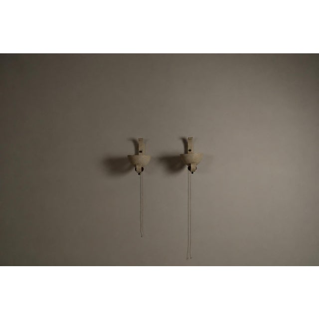 A decorative pair of french wall uplighters dating from circa 1950. each lamp features an expressive curved iron frame...