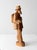Hand-carved wood figure of a traveling peddler, rendered with expressive, faceted carving and a warm, natural tone. The...