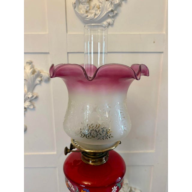 An antique Victorian brass oil lamp with cranberry glass font, raised on a finely cast Corinthian column with fluted stem...
