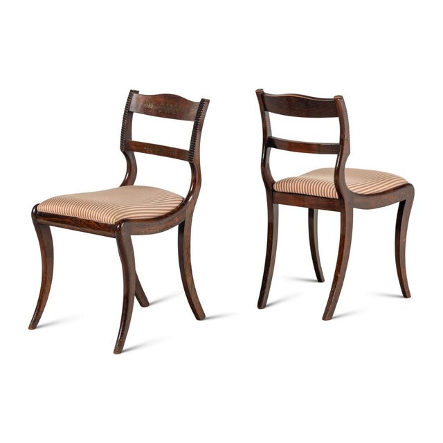 A handsome set of eight English Regency side chairs, each with a gently arched crest rail and shaped mid rail, both inlaid...