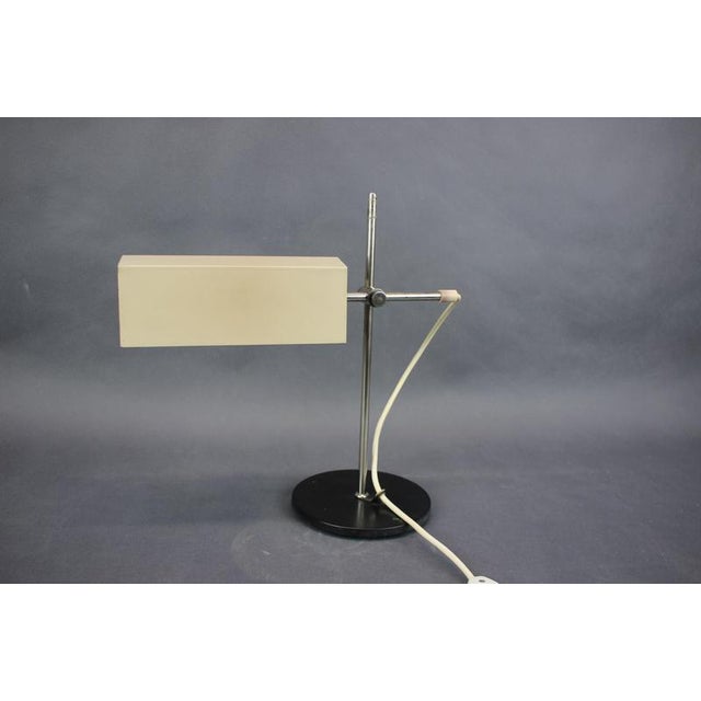 Minimalist German table lamp manufactured during the 1970s. The lamp features a geometric rectangular metal shade combined...