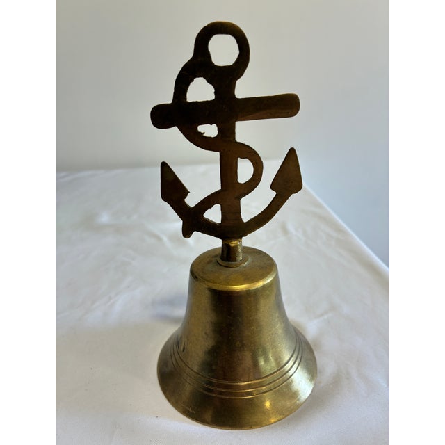 A vintage brass ship's bell finished with a nautical anchor and rope motif finial and banded ring detailing around the...
