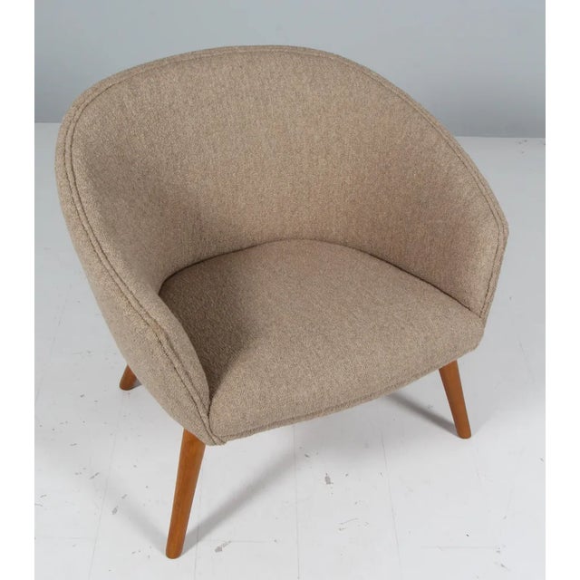 Curved-back lounge chair with splayed stained beech legs and new upholstered with boucle. Designed by Nanna Ditzel and...