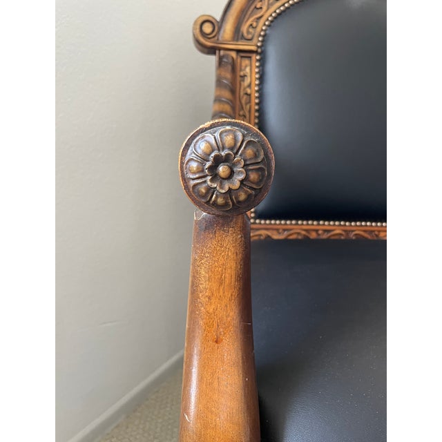 Stunning carved hardwood throne-style armchair with black leather upholstery and brass nailhead trim detail. Elaborately...